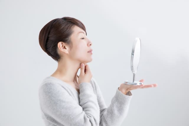 鏡を見ながら首元の肌をチェックする女性