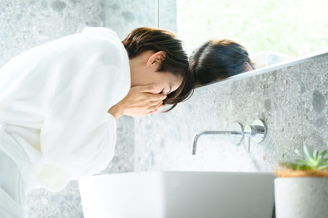 洗面台で水をすくって洗顔する女性