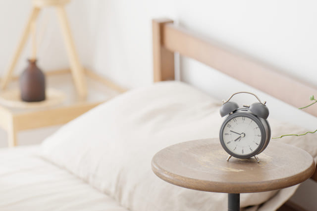 ベッドサイドテーブルに置かれた目覚まし時計と観葉植物