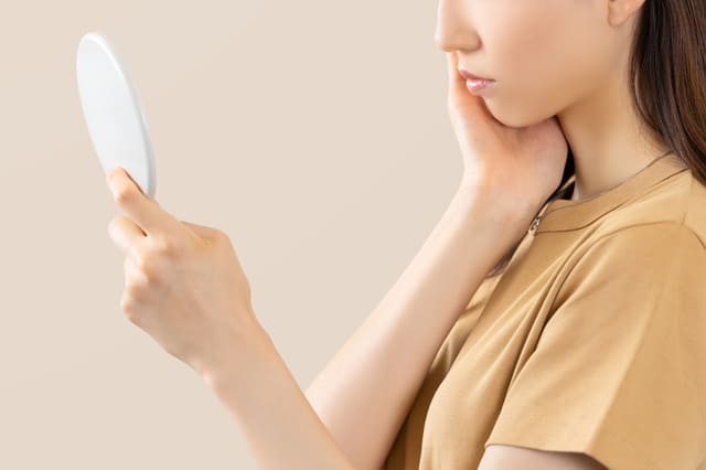 手鏡を持ち頬を押さえて肌をチェックしている女性の横顔