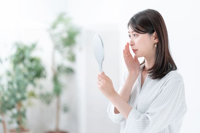 鏡を見ながら肌の状態をチェックする女性