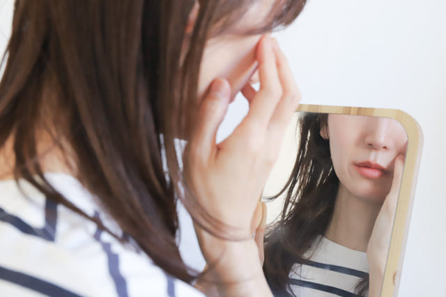 鏡を見ながら肌の状態をチェックする女性