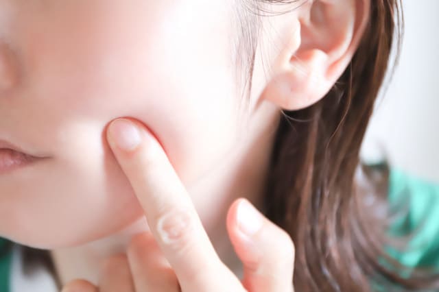頬を指で押さえて肌の状態をチェックする女性