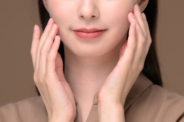 両手で頬に触れる女性の口元アップ